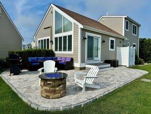 Ein Haus mit einer Terrassenanlage, die einen Steinkamin, Sitzmöglichkeiten im Freien und einen weißen Zaun zeigt.