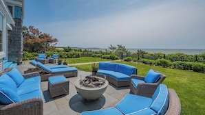 An outdoor patio with blue cushioned seating, a fire pit, and a view of the ocean. - Craigville Long Beach Beachfront rental home. On private beach. RPMS029 (Centerville)