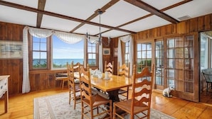 A wooden dining room with a large table and chairs, large windows with ocean views, and a chandelier. - Craigville Long Beach Beachfront rental home. On private beach. RPMS029 (Centerville)