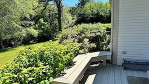 Eine Holzterrasse mit einer Bank, umgeben von üppiger Vegetation und Bäumen.