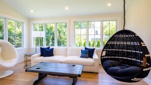 A modern living room with a white sofa, a hanging chair, and a coffee table. - Dazzling High End Home with Heated Pool, Spa and Guest House RPAM013 (East Dennis)