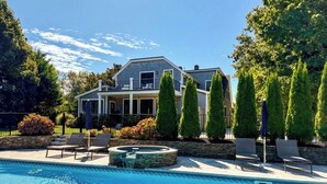 A house with a swimming pool, lounge chairs, and a stone fire pit. - Dazzling High End Home with Heated Pool, Spa and Guest House RPAM013 (East Dennis)