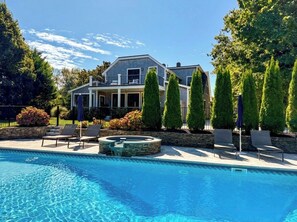 A house with a swimming pool, lounge chairs, and a stone fire pit.