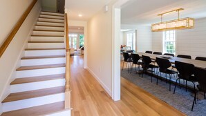 A modern interior with a wooden staircase, a dining area with a long table and chairs, and a chandelier. - Dazzling High End Home with Heated Pool, Spa and Guest House RPAM013 (East Dennis)