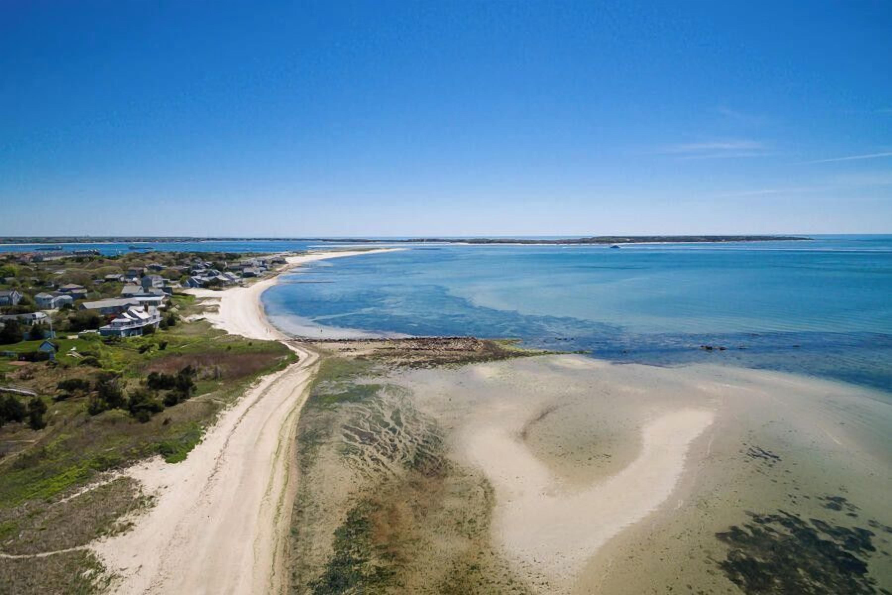 A coastal area with a sandy beach, a clear blue sky, and a few buildings along the shore.