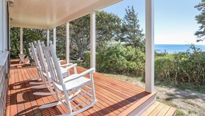 Eine Holzterrasse mit weißen Schaukelstühlen mit Blick auf einen Strand.