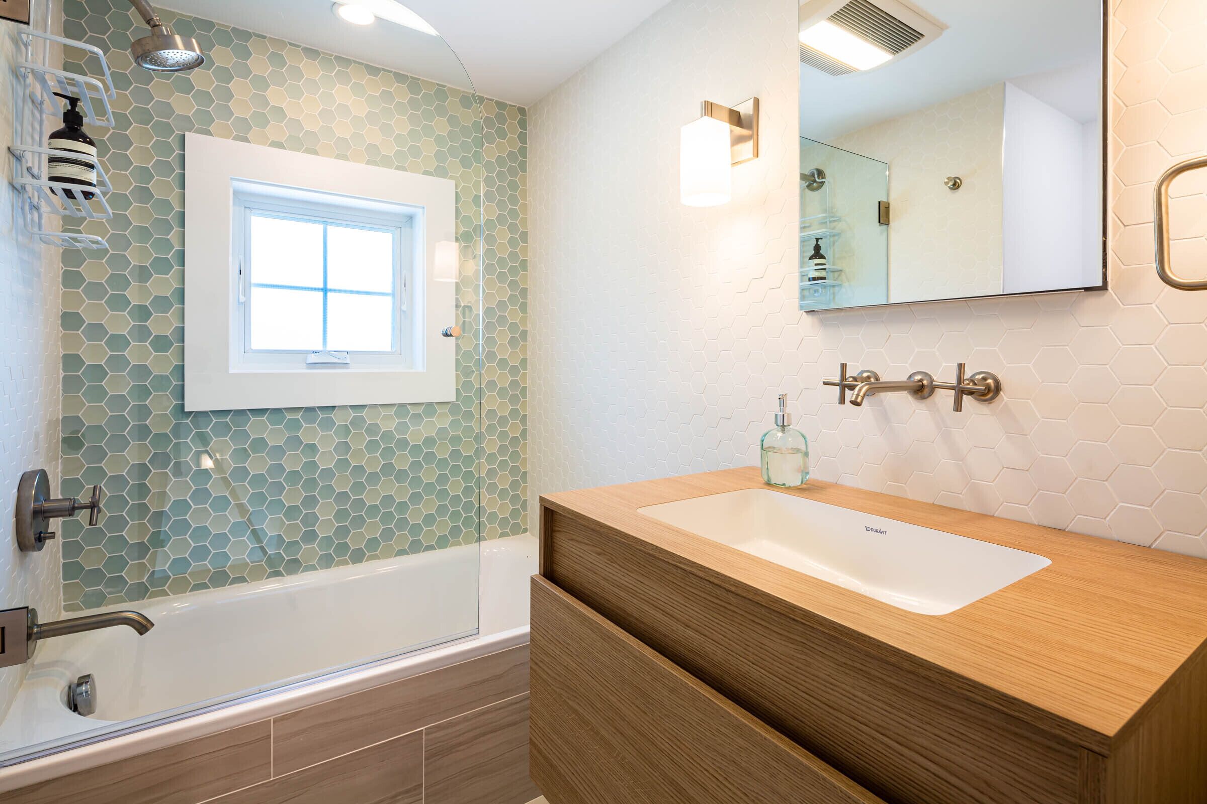 Une salle de bain avec une baignoire, un meuble-lavabo en bois, un miroir et une fenêtre.