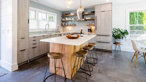 A modern kitchen with a large island, bar stools, and a dining area with a table and chairs. - Exquisite 3 bedroom home in a great location! RPSH005 (Provincetown)