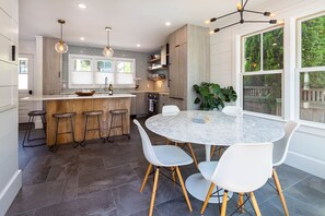 A modern kitchen with a central island, bar stools, and a round dining table with chairs.