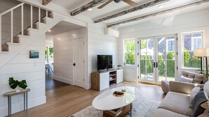 A spacious living room with a wooden staircase, a large window, and a cozy seating area. - Exquisite 3 bedroom home in a great location! RPSH005 (Provincetown)