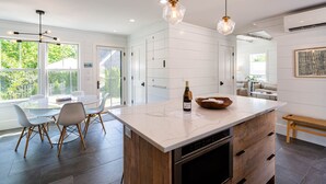 A modern kitchen with a large island, white cabinetry, and a dining area with chairs and a table. - Exquisite 3 bedroom home in a great location! RPSH005 (Provincetown)