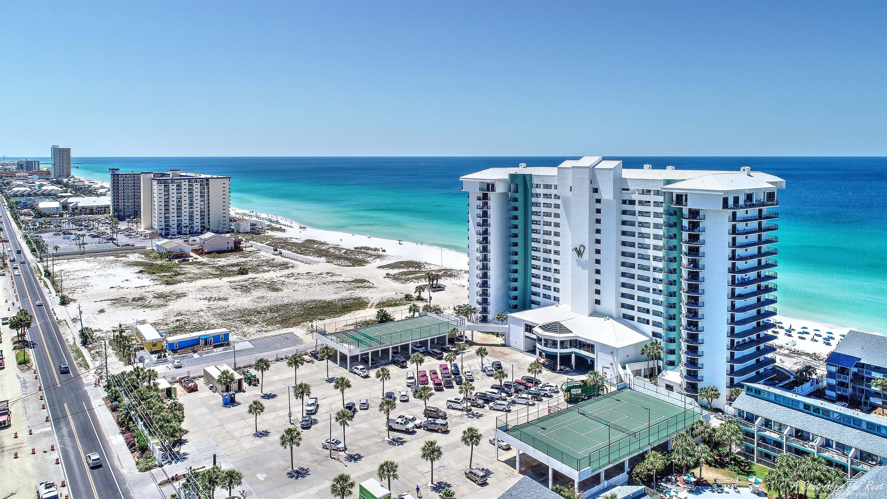Ein hoch aufragendes Hotel mit Blick auf den Strand, einem Parkplatz und einem Tennisplatz.