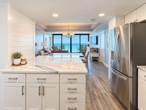 A modern kitchen with a large island, stainless steel appliances, and a view to the outside.