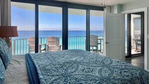 Un dormitorio con una cama grande, un ventilador de techo y vistas al océano a través de amplias ventanas.
