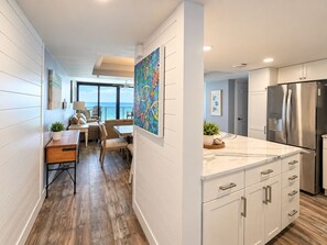 A modern kitchen with white cabinetry, a stainless steel refrigerator, and a large island with a marble countertop.