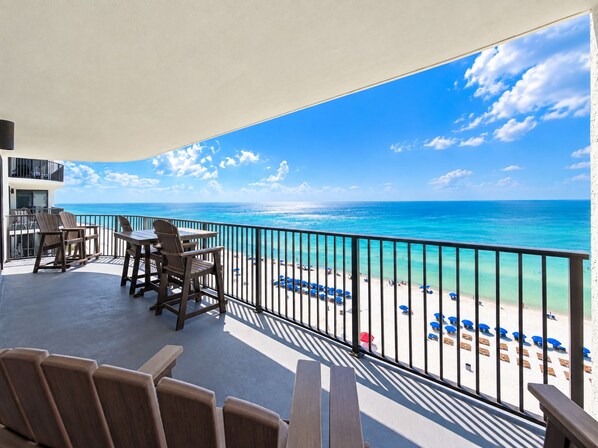 A balcony with a view of the beach, outdoor seating, and a railing.