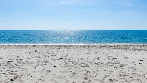 Una playa con cielo despejado y mar tranquilo.