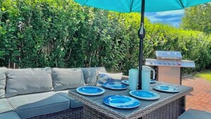 Un patio al aire libre con una mesa de comedor lista para cuatro personas, rodeado de asientos acolchados.