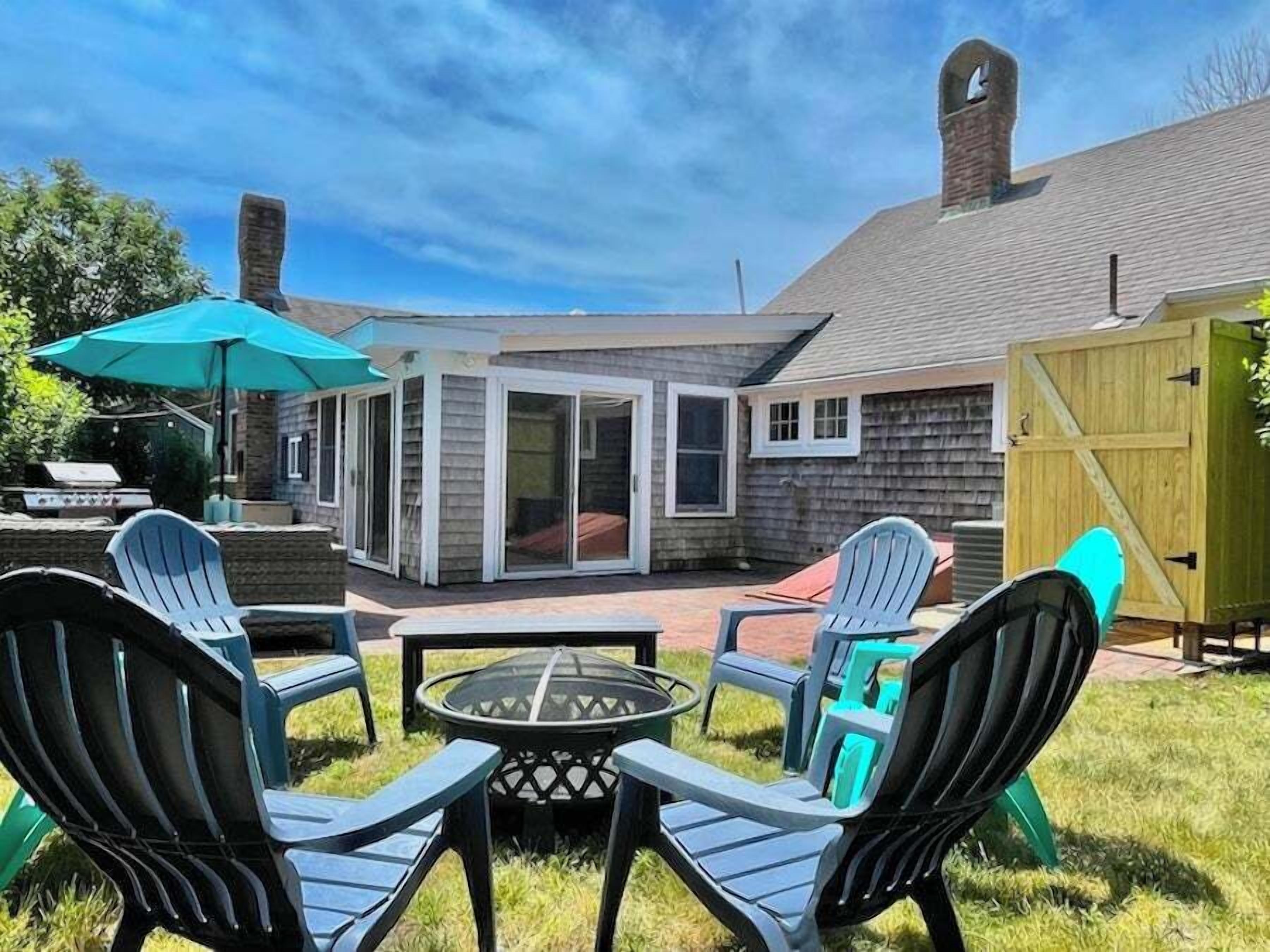 A patio with four Adirondack chairs, a glass-top table, and a blue umbrella.