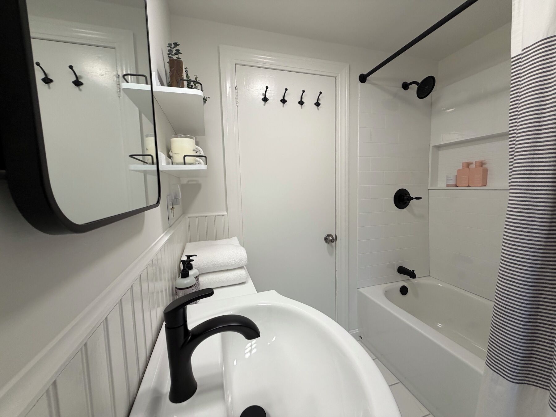 A bathroom with a white sink, black faucet, a mirror, a towel rack, a shower curtain, and a bathtub.