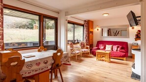 A cozy living room with a red sofa, wooden dining table, and chairs. - 20m from ski slopes, 2nd floor, balcony, fireplace or stove, tv, 48m², Méribel-Mottaret (Méribel - Les Allues)
