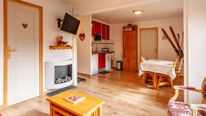 A living room with a fireplace, a dining table, and a kitchen in the background. - 20m from ski slopes, 2nd floor, balcony, fireplace or stove, tv, 48m², Méribel-Mottaret (Méribel - Les Allues)