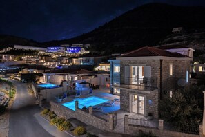 A multi-story building with a swimming pool, outdoor seating, and a view of the surrounding hillside.