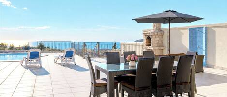 A rooftop terrace with a pool, lounge chairs, and a dining area with wicker furniture and a table.