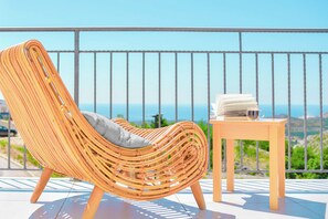 A wicker chair with a cushion on a balcony with a table and books, overlooking a coastal view. - Luxury Villa Price with private heated pool-near Dubrovnik. Sleeps 6 comfortably (Ivanica - Ravno)