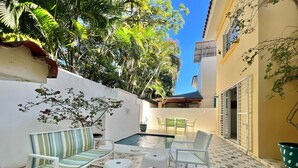 Un patio con piscina, sillas blancas, un sofá a rayas y una mesita.