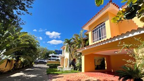 Un edificio residencial con entrada pavimentada, porche cubierto y vista a una calle con otros edificios.