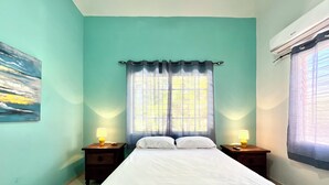 Un dormitorio con una cama, dos mesitas de noche con lámparas, una ventana con cortinas y un cuadro en la pared.