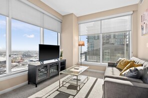 Relax in this stylish living room with a large flat-screen TV, comfortable sofa, and floor lamp, offering a view of the city.