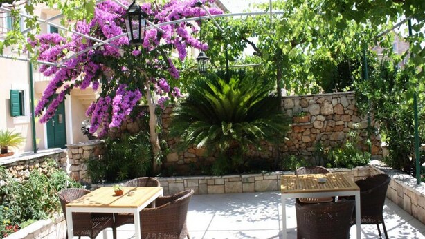 Un patio al aire libre con mobiliario de mimbre, un muro de piedra y coloridas flores de buganvilla moradas.