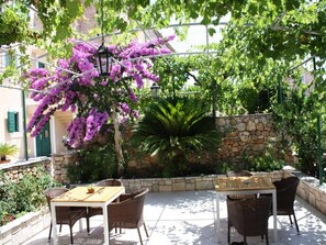 Un patio al aire libre con mobiliario de mimbre, un muro de piedra y coloridas flores de buganvilla moradas.