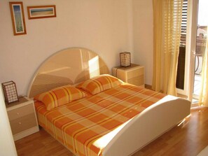 Un dormitorio con cama, dos mesitas de noche, una ventana con cortinas y dos cuadros en la pared.