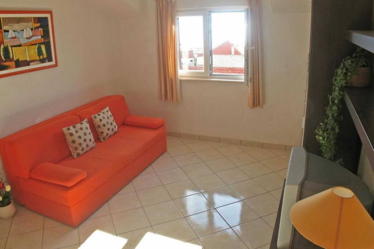 A living room with a red sofa, a small table, a window with curtains, and a painting on the wall.