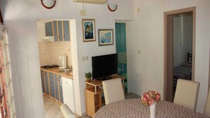 Un espacio habitable compacto con kitchenette, comedor con mesa y sillas, televisor y un baño pequeño visible a través de una puerta abierta.