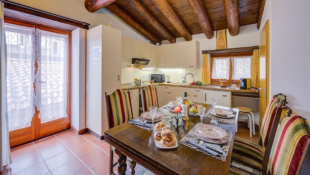 A dining area with a wooden table set for a meal, striped chairs, and a kitchen in the background. - Ca' Pinina (Lugano)
