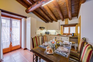 A dining area with a wooden table set for a meal, striped chairs, and a kitchen in the background. - Ca' Pinina (Lugano)
