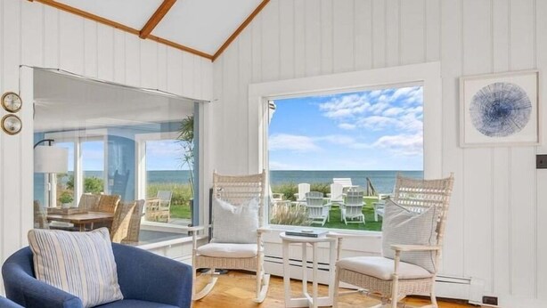 Una habitación con una ventana grande que da a una playa, muebles de mimbre y un sofá azul.