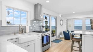 Una cocina moderna con armarios blancos, una estufa a gas y un amplio ventanal con vistas al mar.