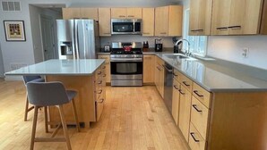 Una cocina moderna con armarios de madera, electrodomésticos de acero inoxidable y una isla central con taburetes de bar.