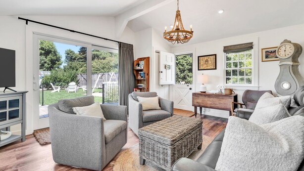 A spacious living room with a large window, a chandelier, and a wooden coffee table. - Time and Tide Cottage - A Barnstable Village Retreat RPAM020 (Barnstable)
