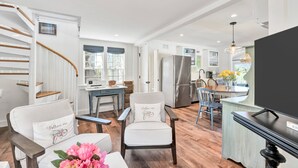 A modern kitchen with a built-in refrigerator, a dining area with a wooden table and chairs, and a staircase with wooden railings. - Time and Tide Cottage - A Barnstable Village Retreat RPAM020 (Barnstable)