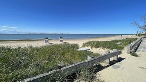 A beach with a wooden boardwalk, grassy dunes, and a clear blue sky. - Time and Tide Cottage - A Barnstable Village Retreat RPAM020 (Barnstable)
