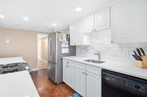 Enjoy cooking in this well-equipped kitchen with a refrigerator, dishwasher, and white cabinetry.
