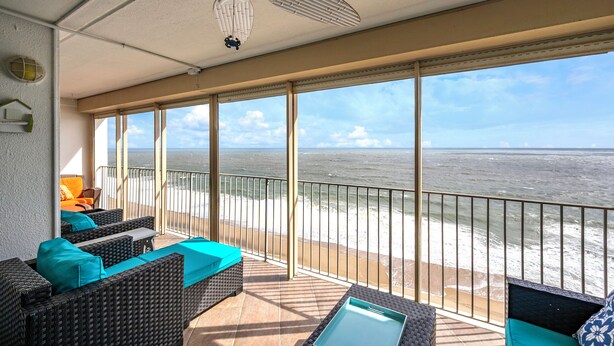 A balcony with wicker furniture, a ceiling fan, and a view of the ocean.