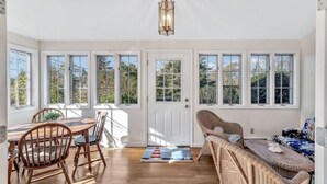 A bright room with large windows, a dining table with chairs, a wicker sofa, and a hanging light fixture. - Private Beach Front Chatham Rental Close To Everything RPAM054 (Chatham)