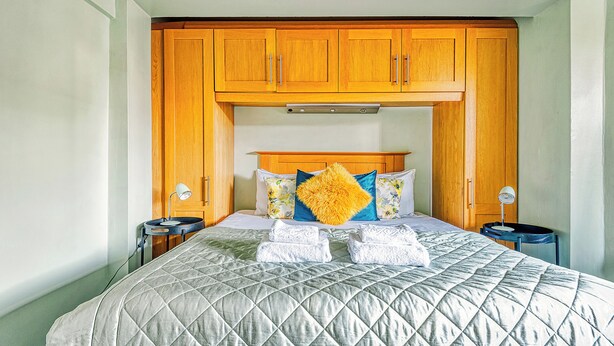 Un lit bien fait, avec une couverture matelassée, une tête de lit en bois et deux lampes de chevet.